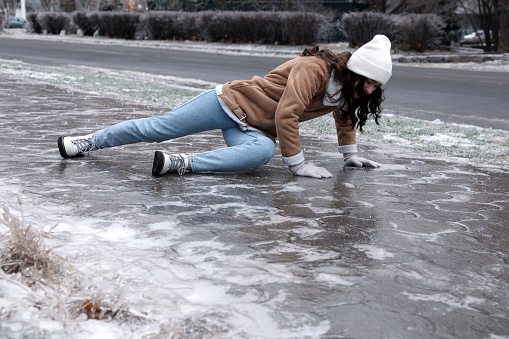 Mujer joven tratando de ponerse de pie después de caer sobre el pavimento helado resbaladizo al aire libre photo