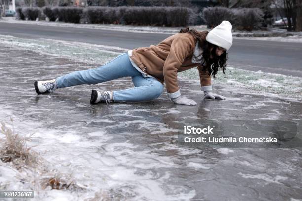 Young Woman Trying To Stand Up After Falling On Slippery Icy Pavement Outdoors Stock Photo - Download Image Now