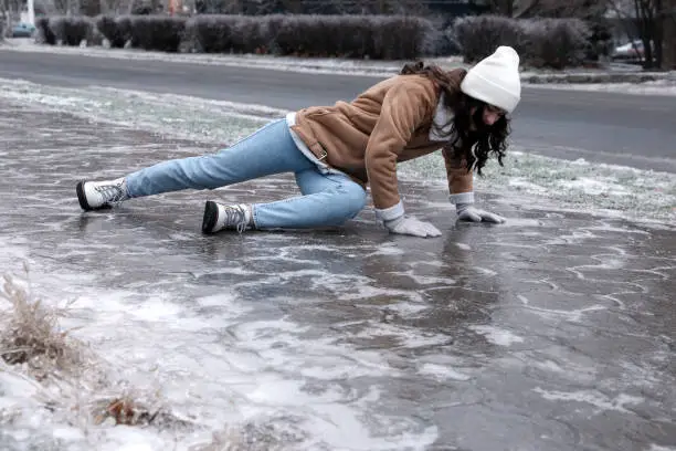 Photo of Young woman trying to stand up after falling on slippery icy pavement outdoors