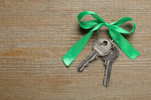 Keys with green bow on wooden table, top view and space for text. Housewarming party