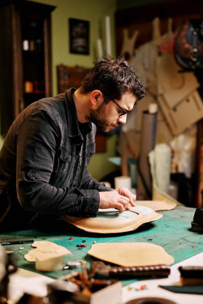 istock Portrait of leather craftsman makes a leather motorcycle seat at table in workshop studio 1441236415