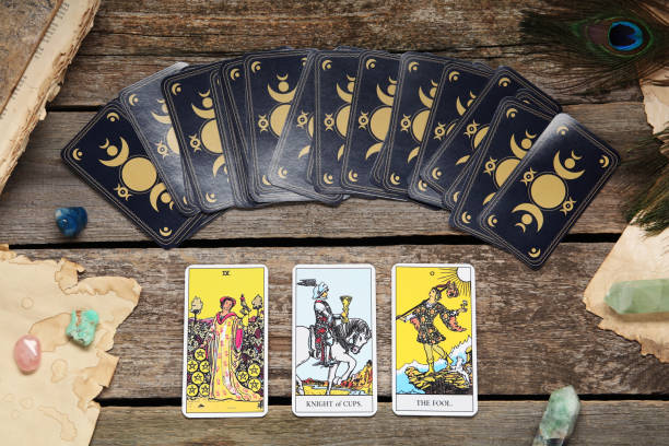 istock Tarot cards, peacock feather, gemstones and old book on wooden table, flat lay 1441237007
