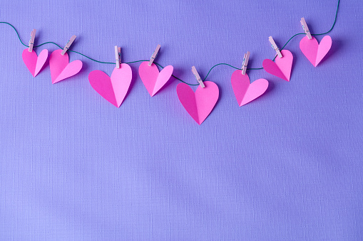 Pink paper cut hearts hanging on a clothesline with wooden clothespins. Space for copy.