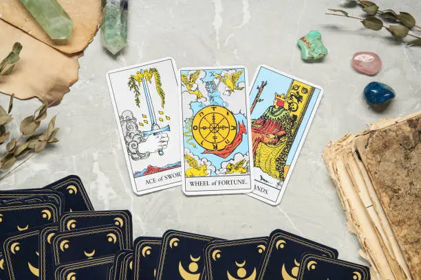 Tarot cards with gemstones and old book on grey table, flat lay