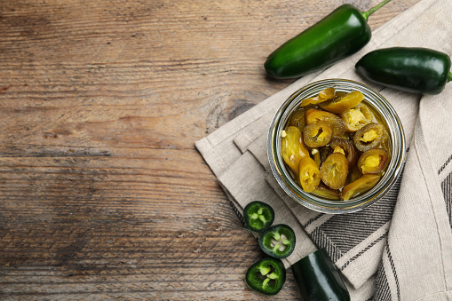 Fresh and pickled green jalapeno peppers on wooden table, flat lay. Space for text