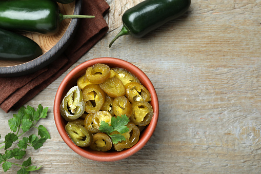 Fresh and pickled green jalapeno peppers on wooden table, flat lay. Space for text
