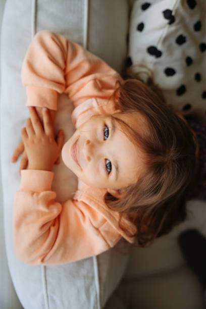 ritratto ravvicinato di una bambina carina che guarda la macchina fotografica e sorride gentilmente nel soggiorno a casa - 4 of a kind foto e immagini stock