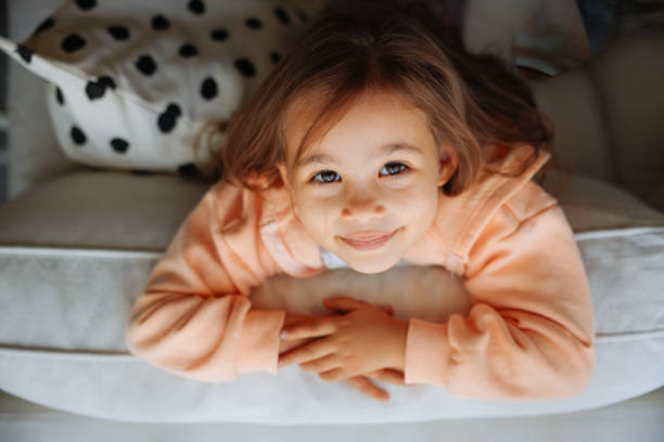 ritratto ravvicinato di una bambina carina che guarda la macchina fotografica e sorride gentilmente nel soggiorno a casa - 4 of a kind foto e immagini stock