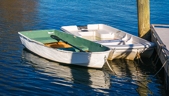 Two small white rowboats are moored to a dock on a November afternoon at the Cotuit Town Dock in  Cotuit, Massachusetts on Cape Cod.