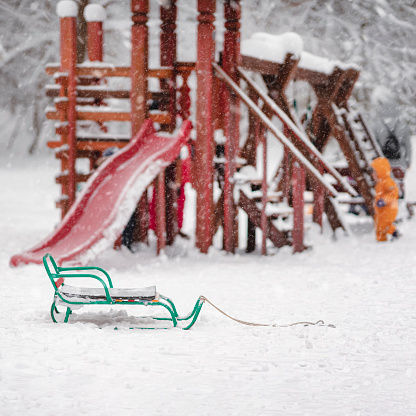 Empty sleds on playground on white fresh snow, park in winter day. Soft blurry selective focus