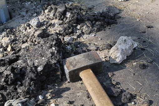 Close-up of big metal steel sledge hammer with wooden handle on cracking old pavement after road breaking. Hard work technical equipment on construction site. Industry tools. Work labor concept