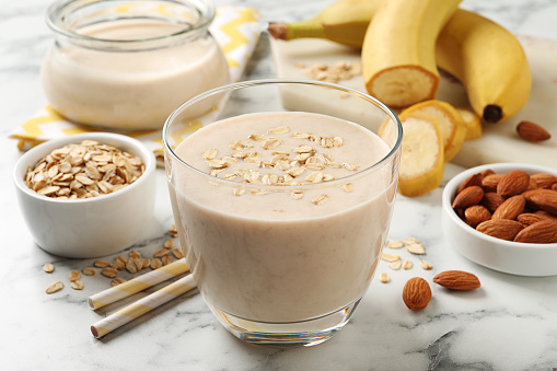 Glass of tasty banana smoothie with oatmeal on white marble table