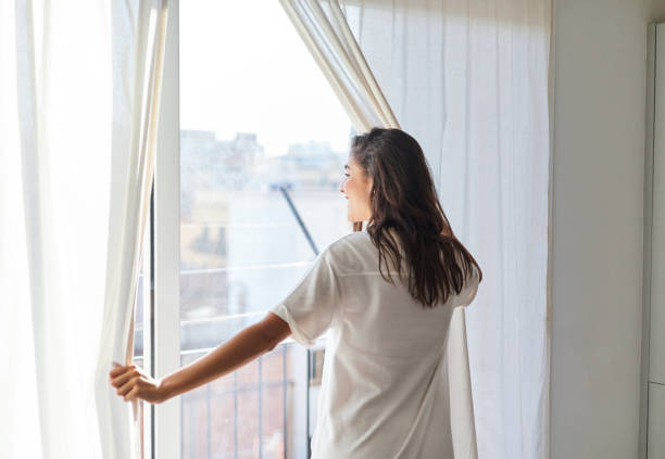 istock Woman opening window curtains at home in morning, back view 1441247151