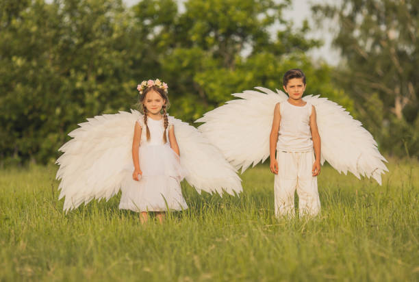 Two angels with white wings on green grass. Blonde girl in dress and brunette boy on summer sunset background Two angels with white wings on green grass. Blonde girl in dress and brunette boy on summer sunset background teenager couple child blond hair stock pictures, royalty-free photos & images