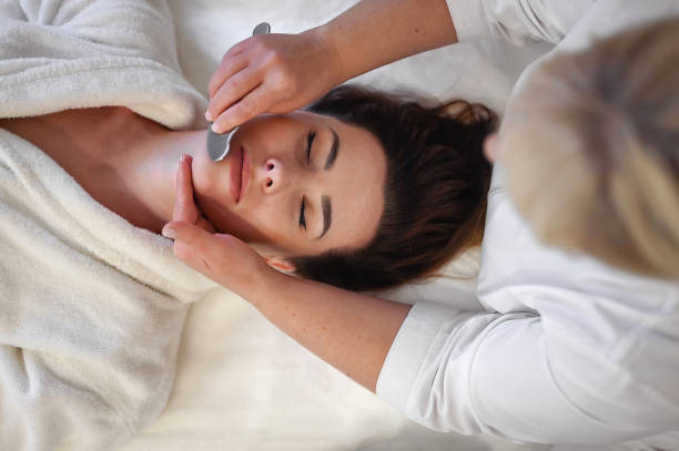 vue d’en haut. portrait d’une femme recevant un massage facial avec l’outil gua sha dans un salon de beauté. - massaging spa treatment stone massage therapist photos et images de collection