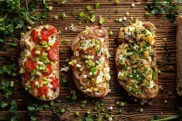 Sandwiches with scrambled eggs and vegetables,  sprinkled with  fresh herbs on a wooden plank, top view