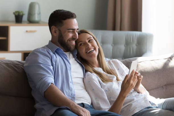 Pretty laughing couple relaxing on sofa using smartphone