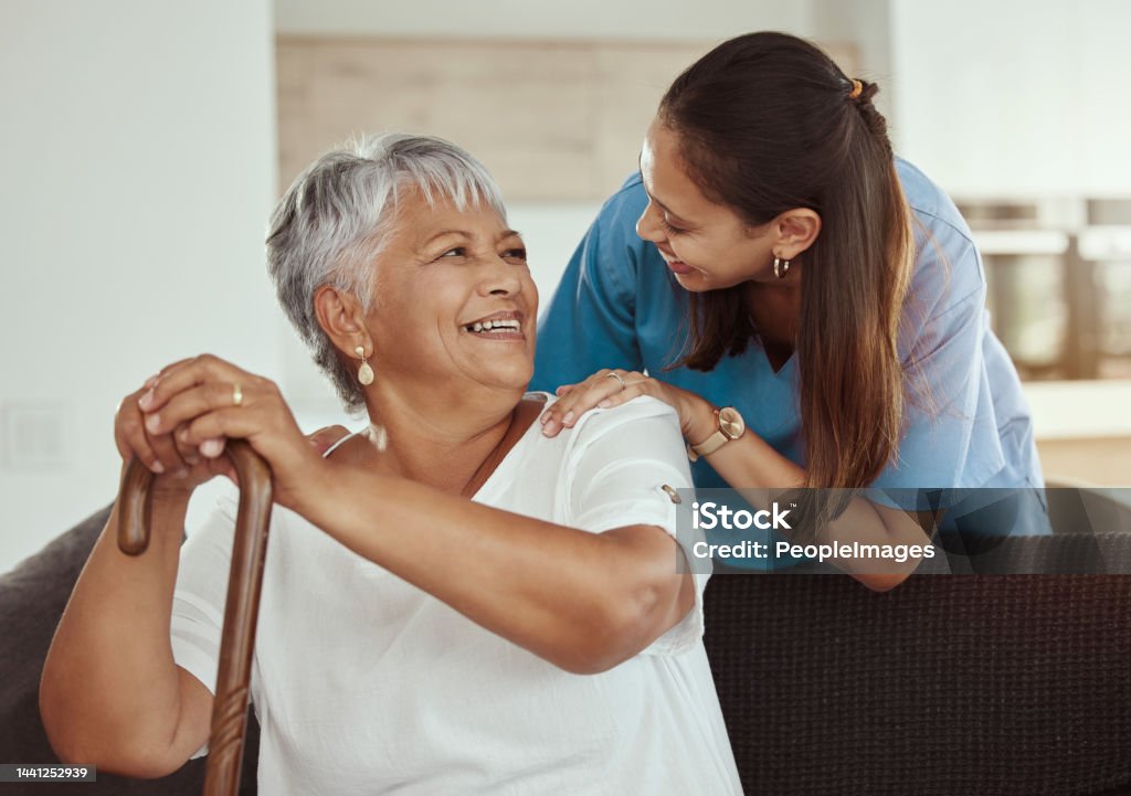 Happy, relax and senior woman with caregiver smile while sitting on a living room sofa in a nursing home. Support, help and professional nurse or healthcare worker helping elderly lady or patient Nursing Home Stock Photo
