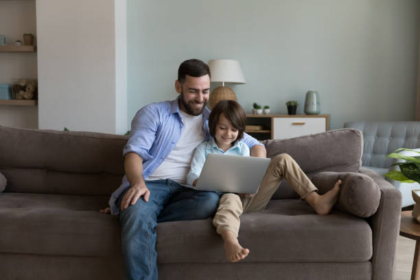 istock Dad and son sit on sofa enjoy weekend use laptop 1441252971