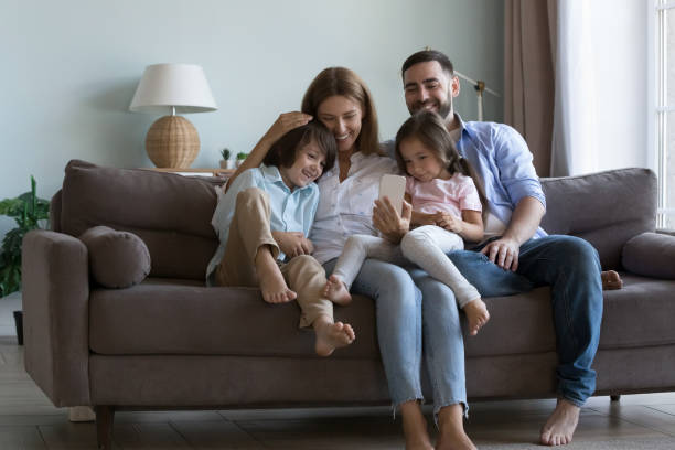 istock Couple with little children sit on couch using cellphone 1441253390
