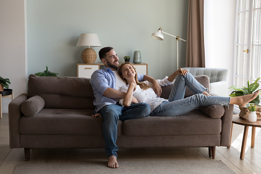 Relaxed couple in love enjoy conversation resting on sofa in fashionable living room, share dreams, planning future and children, spend time at modern home. Daydreams, romantic relations, date concept