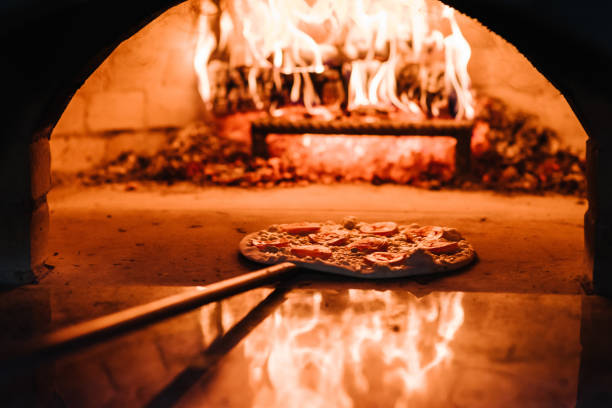 шеф-повар кладет маргариту, четыре сыра или мясную пиццу на лопату в духовку. дровяная печь для приготовления и выпечки пиццы. итальянская т - wood fire oven стоковые фото и изображения