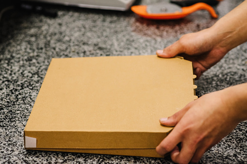 The courier holding a cardboard pizza box. Brown box for shipping and delivery. Food order service and delivering concept. Fast food orders from customer at home. Place for text and advertising.