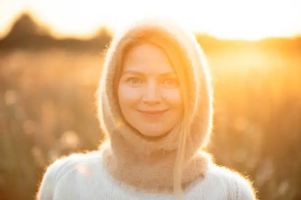 Portrait Of Young Pretty Caucasian Happy Girl Woman In Woolen Jacket Blouse And Brown knitted bonnet Posing In Early Spring Forest In Sunny Day. Enjoy Outdoor Nature. beautiful young woman smiling. power of women. knitted wear, knitted bonnet, knitwear,