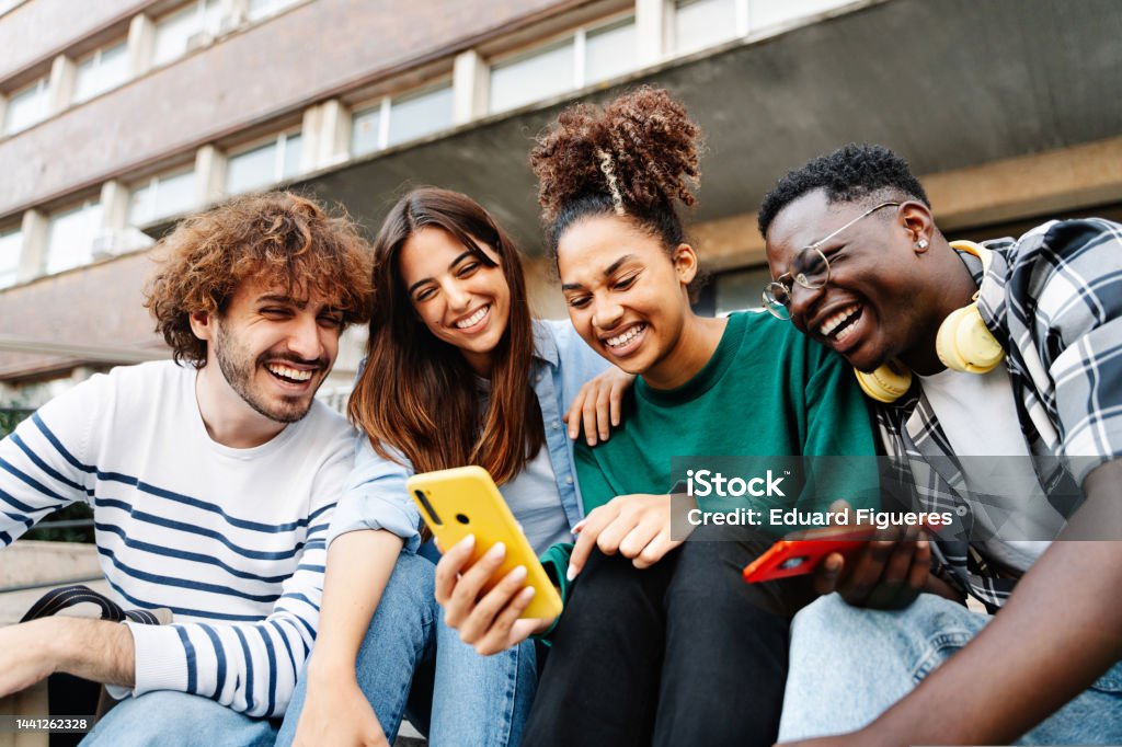 Group of university student friends sitting together using mobile phones to share content on social media Using Phone Stock Photo