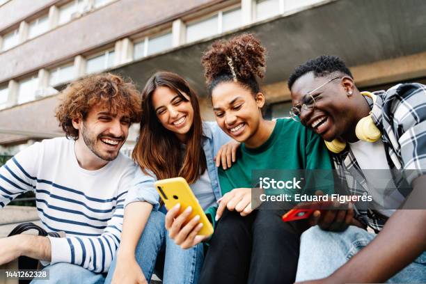 Group Of University Student Friends Sitting Together Using Mobile Phones To Share Content On Social Media Stock Photo - Download Image Now