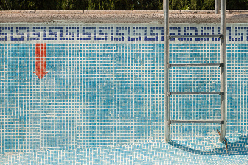 Tiled pool without water with a ladder and a red downward arrow warning sign. Textured background.