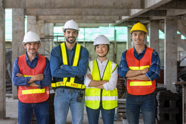 portrait of experienced diversity team of engineer, architect, worker and safety manager smiling together at the construction site in safety vest and helmet - subcontractor imagens e fotografias de stock