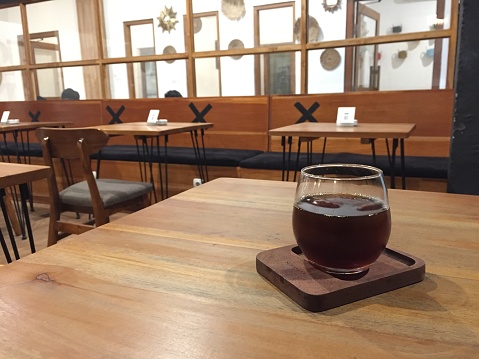 a glass of coffee water which lies on a wooden saucer and around there are empty benches