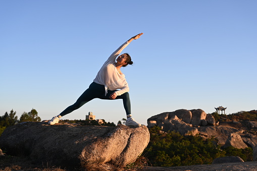 Chinese woman doing yoga poses at sunset on the mountain top