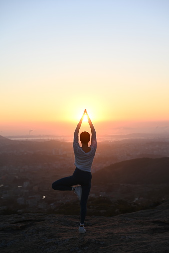 Chinese woman backlit yoga pose on top of mountain