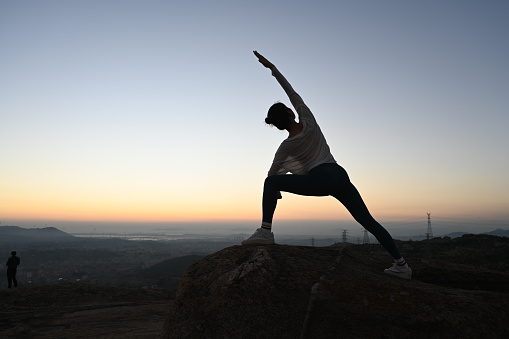 Chinese woman backlit silhouette yoga pose on top of mountain