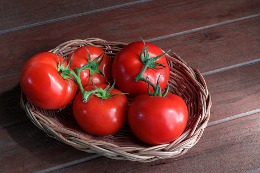 Fresh tomatoes, red peppers, carrots, and radish in a basket on dark wooden background