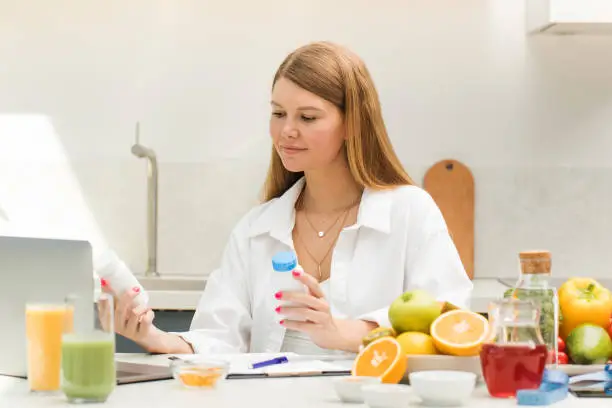 Photo of A nutritionist holds jars of vitamins in front of a laptop while sitting at a table