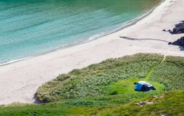 Scottish camping spot,stunning sands,calm Atlantic azure sea,sunny summertime morning,grass covered,underneath Beinn Ceannabeinne mountain,beautiful sand,steep grassy slope gives access to beach.