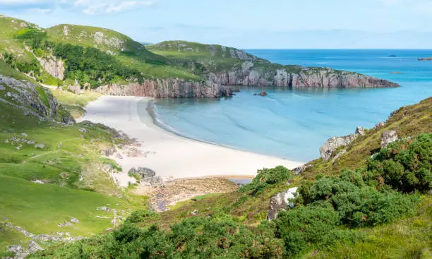 Scottish camping spot,stunning sands,calm Atlantic azure sea,sunny summertime morning,grass covered,underneath Beinn Ceannabeinne mountain,beautiful sand,steep grassy slope gives access to beach.