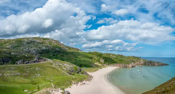 Scottish camping spot,stunning sands,calm Atlantic azure sea,sunny summertime morning,grass covered,underneath Beinn Ceannabeinne mountain,beautiful sand,steep grassy slope gives access to beach.