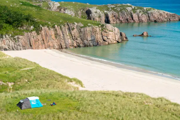 Scottish camping spot,stunning sands,calm Atlantic azure sea,sunny summertime morning,grass covered,underneath Beinn Ceannabeinne mountain,beautiful sand,steep grassy slope gives access to beach.