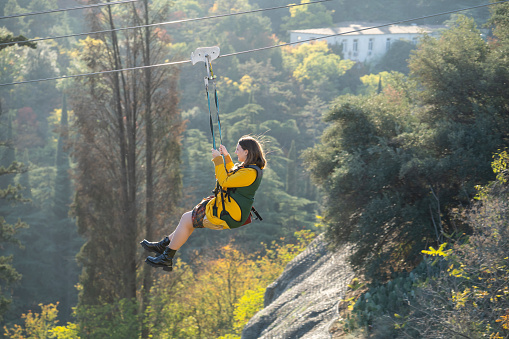 November 05, 2022 Tbilisi Georgia. Woman tourist tied to steel hawser goes down ropeway. Girl participates in extreme attraction going down from high mountain on bungee over picturesque forest