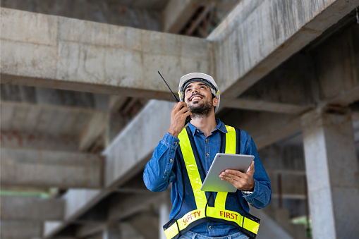 Caucasian engineer with radio walkie talkie in full safety gear is inspecting inside the building structure for investigation over specification and quality control usage