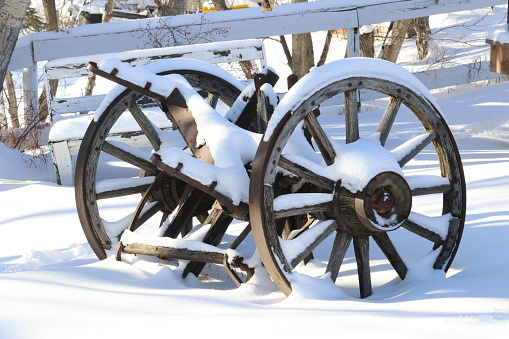 Outdoor winter image of a set of weathered old rustic wooden wagon wheels covered in fresh white snow.