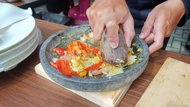 grinding the spices with a mortar and pestle from a stone on a wooden table - mortar and pestle spice seasoning coriander seed imagens e fotografias de stock