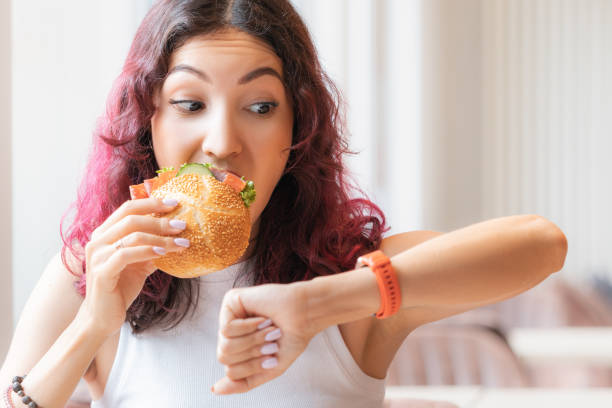 The girl was in a hurry looking at wristwatch and finishing to eat her burger in a fast food cafe The girl was in a hurry looking at wristwatch and finishing to eat her burger in a fast food cafe instant food stock pictures, royalty-free photos & images