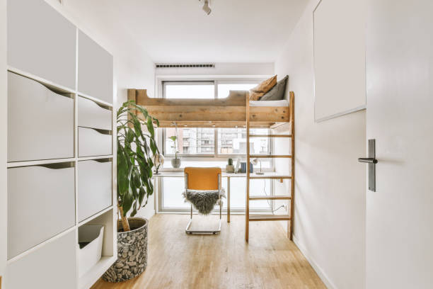The interior of a small bedroom with a single wooden bed on the second tier and a work space under the bed