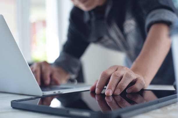istock Closeup of business man working on laptop computer and using digital tablet pc on table at home office 1441313458