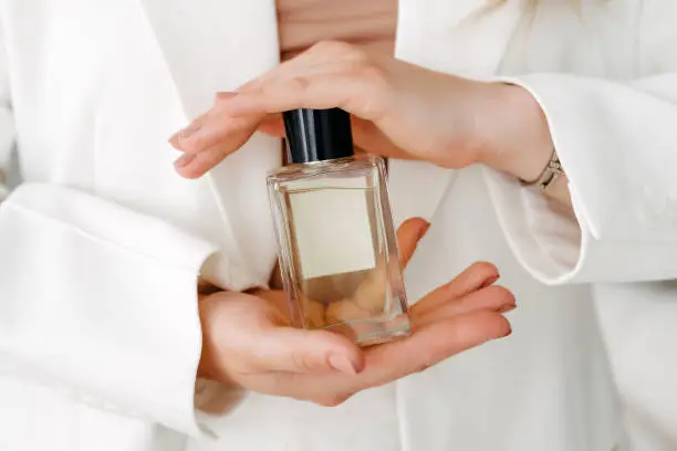 Hands of a beautiful young woman with a bottle of floral perfume on a light background